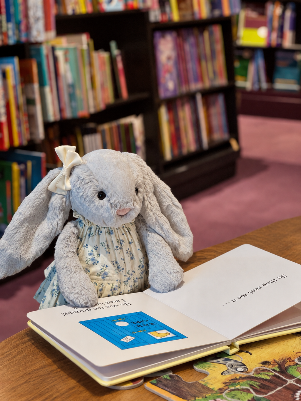 Silver plush bunny wearing a blue floral tiered dress with a cream bow hair clip besides an open book
