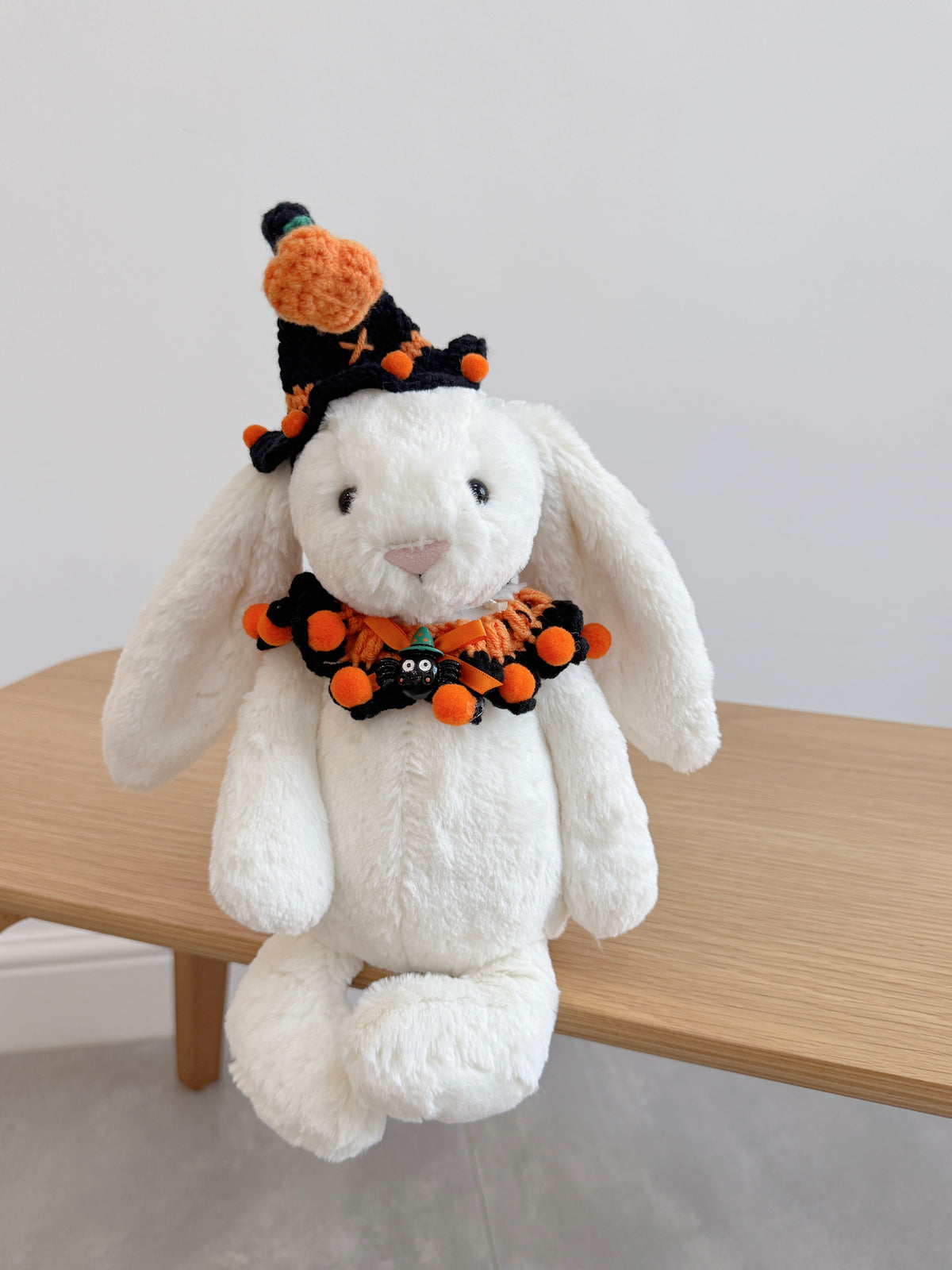 White plush bunny wearing a crochet  Halloween witch hat with pumpkin detail and matching ruffled collar 