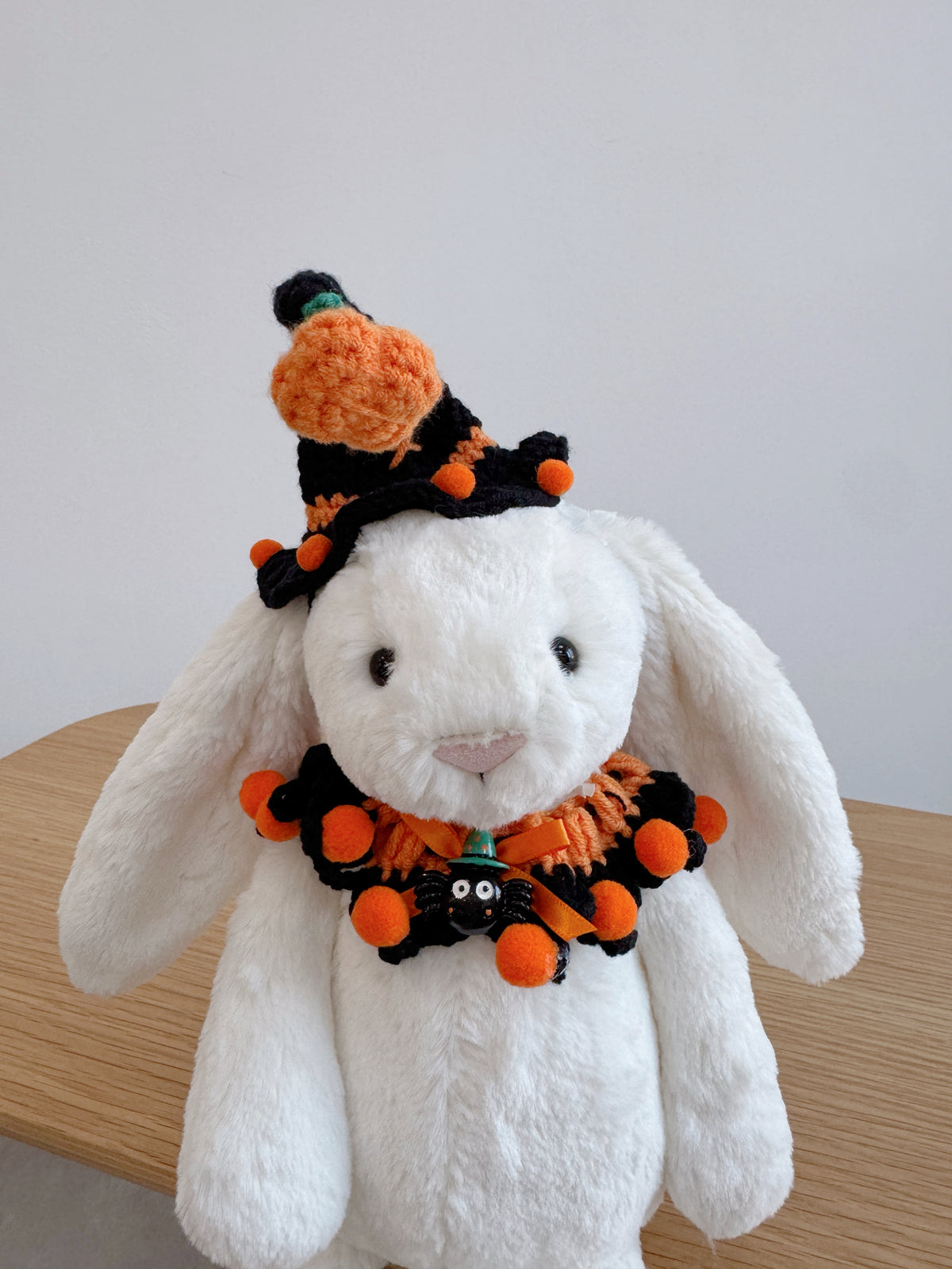 White plush bunny wearing a crochet  Halloween witch hat with pumpkin detail and matching ruffled collar 
