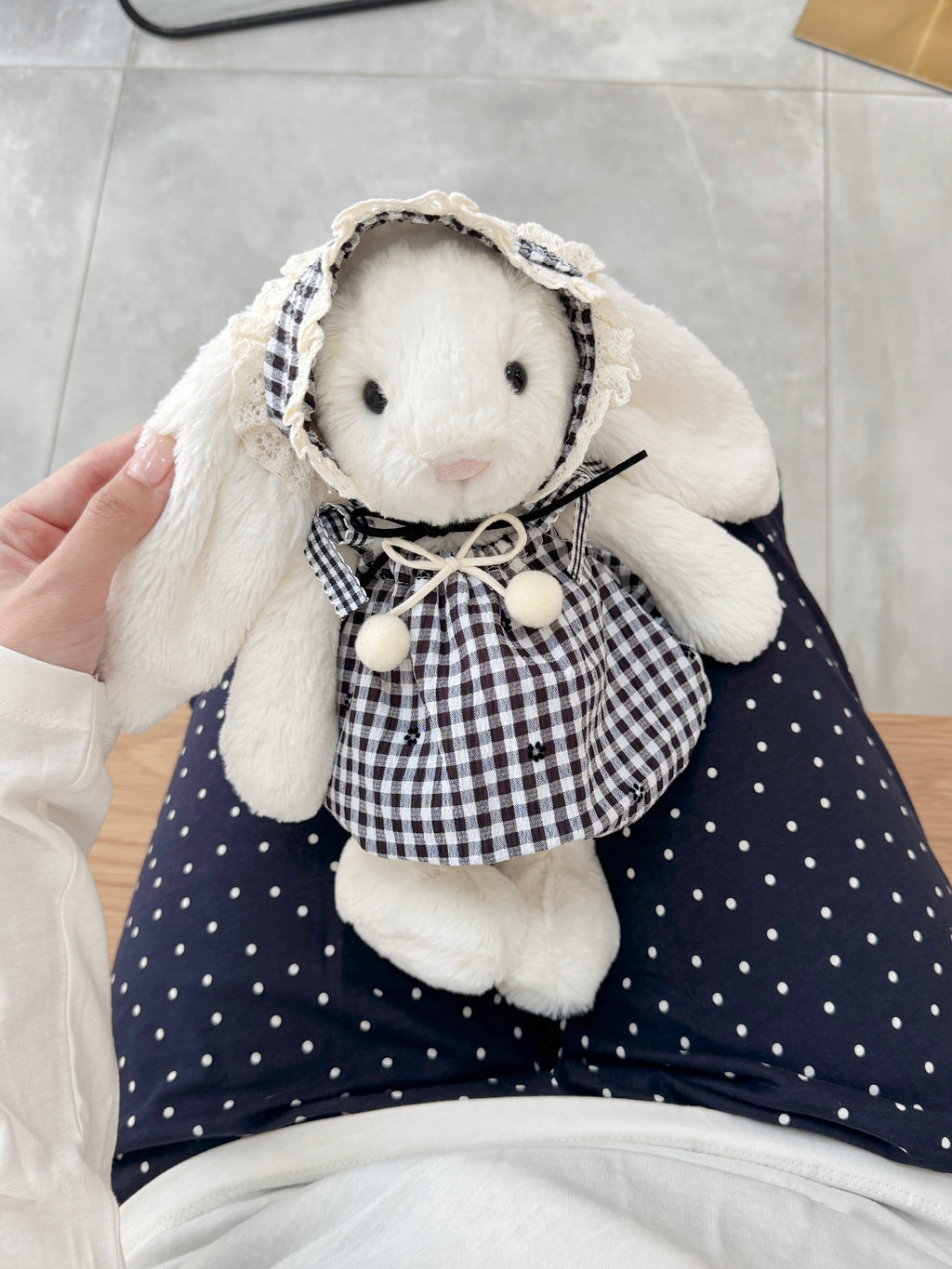 White plush bunny dressed in a black and white gingham outfit with gathered skirt and lace bonnet