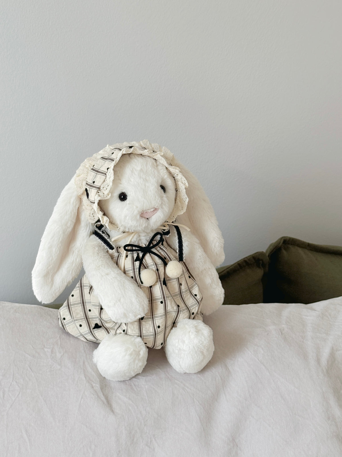 White plush bunny wearing a heart-detail dress with soft pom-poms and matching lace-trimmed bonnet