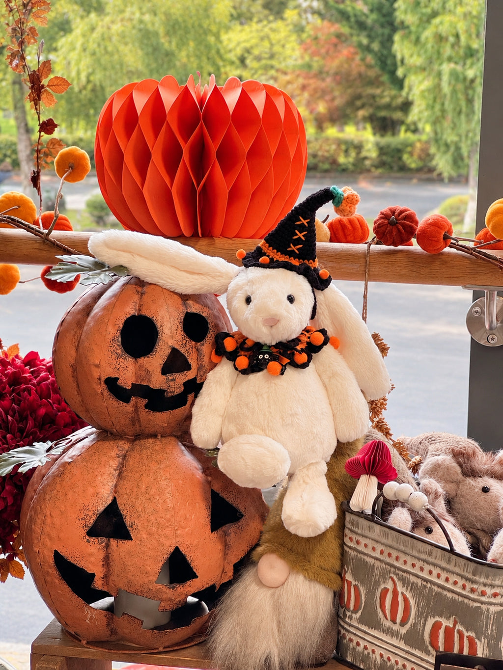 White plush bunny wearing a black and orange Halloween witch hat and matching ruffled collar beside pumpkins