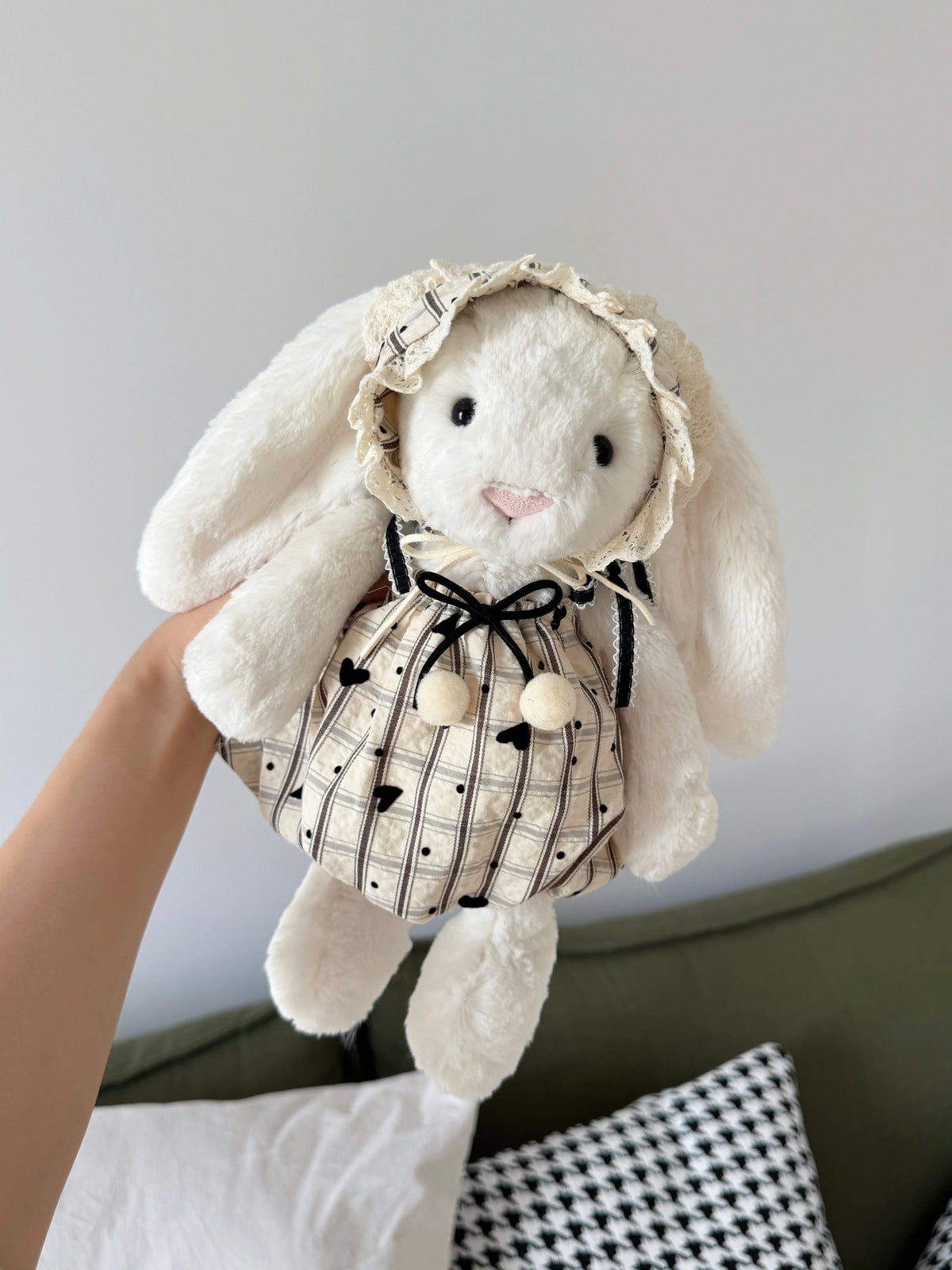 White plush bunny wearing a heart-detail dress with soft pom-poms and matching lace-trimmed bonnet