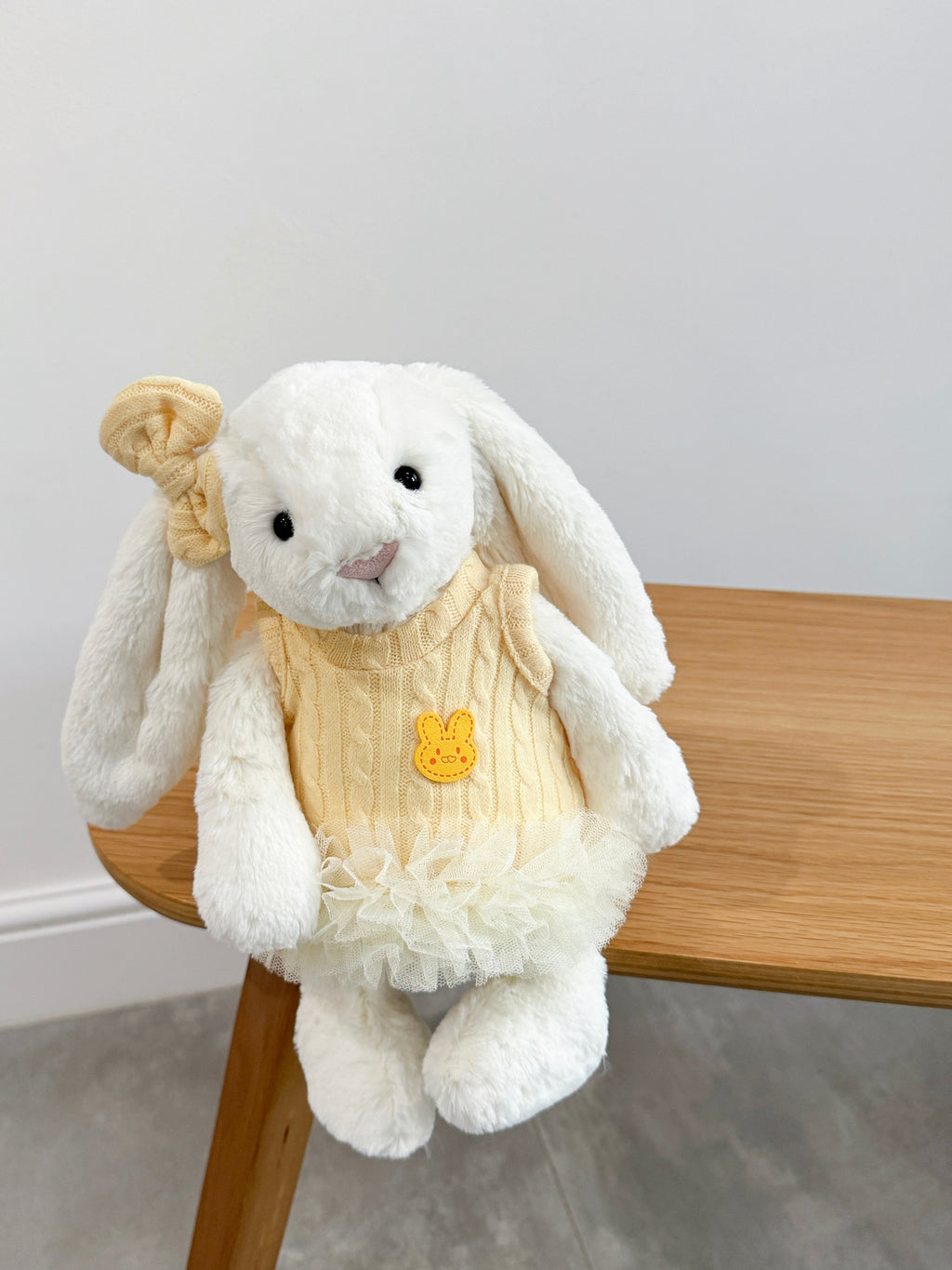 White plush bunny wearing a soft yellow cable knit tutu dress and matching bow