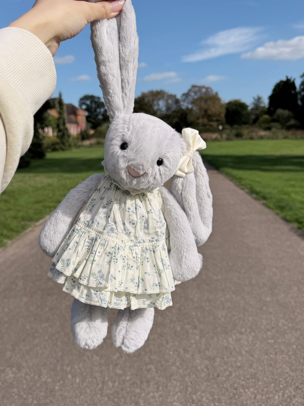 Silver plush bunny wearing a blue floral tiered dress with a cream bow hair clip outdoors