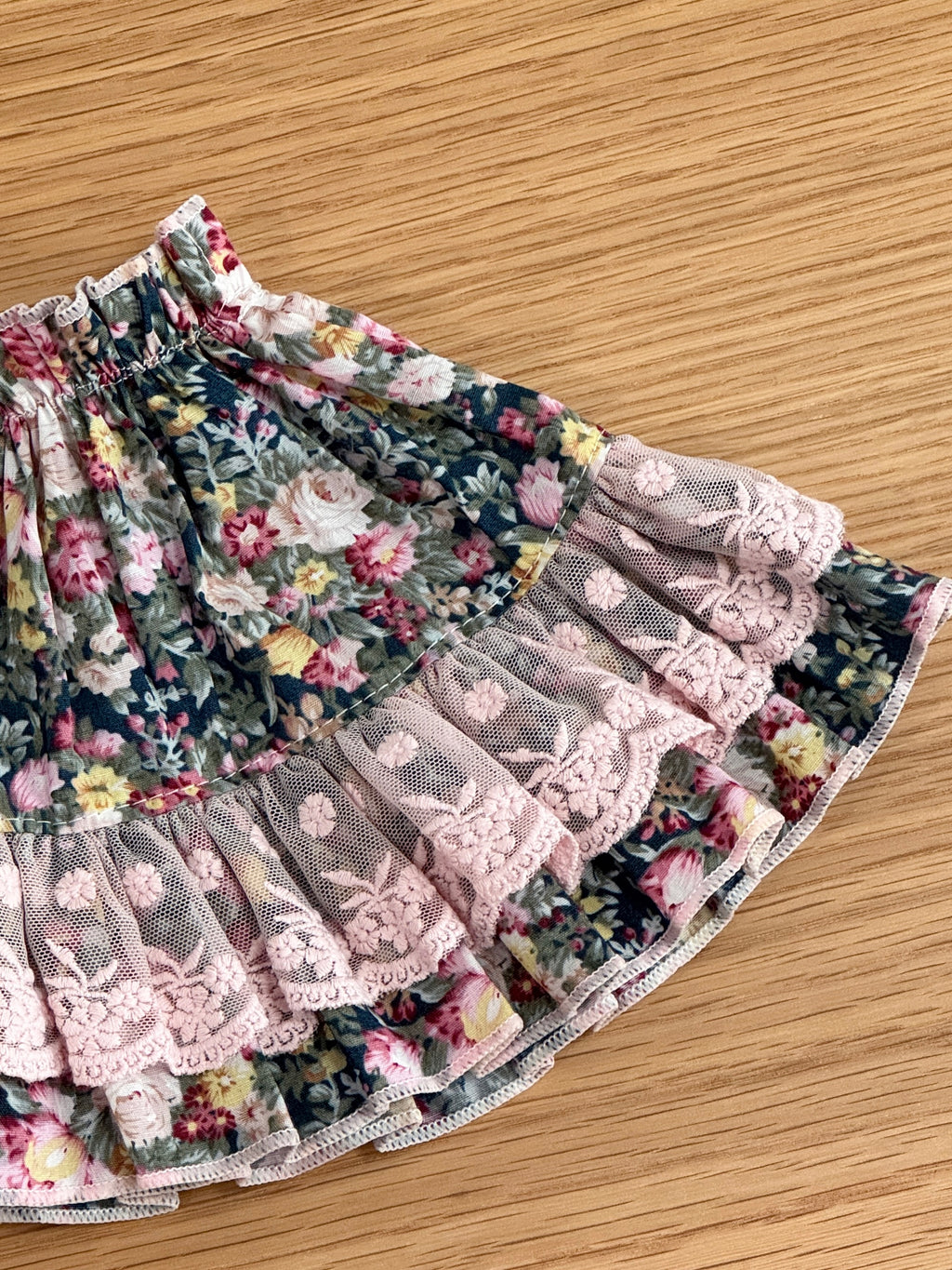 Close-up of pink embroidered lace and layered ruffle detailing on a floral dress for a plush bunny