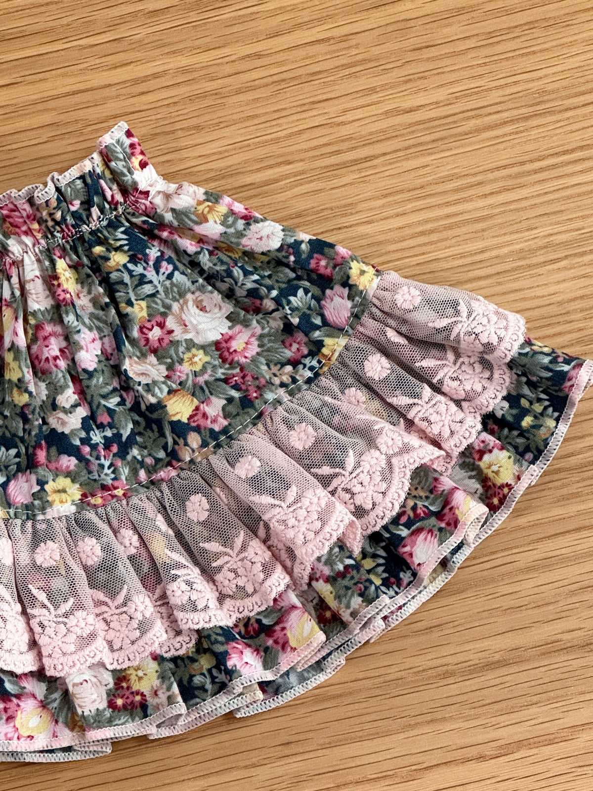 Close-up of pink embroidered lace and layered ruffle detailing on a floral dress for a plush bunny