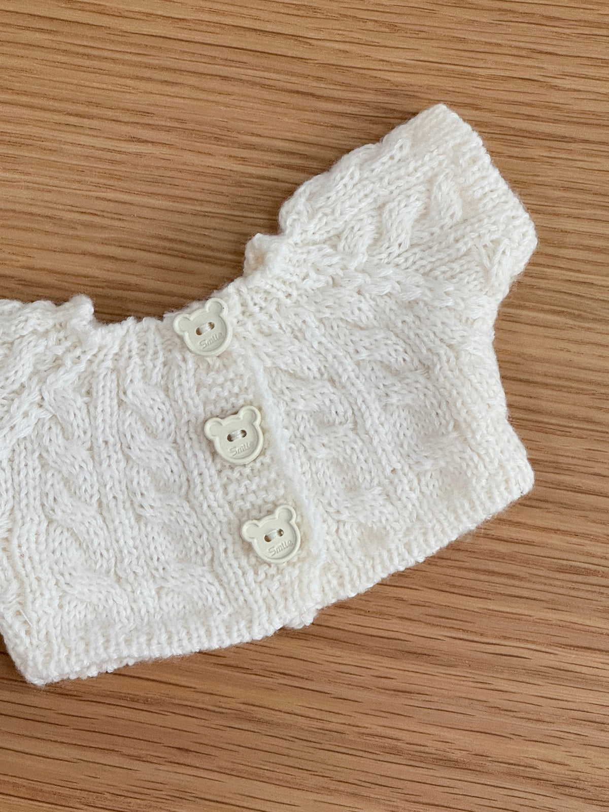 Close-up of cream cable knit plush bunny cardigan with cable pattern and three bear-shaped buttons