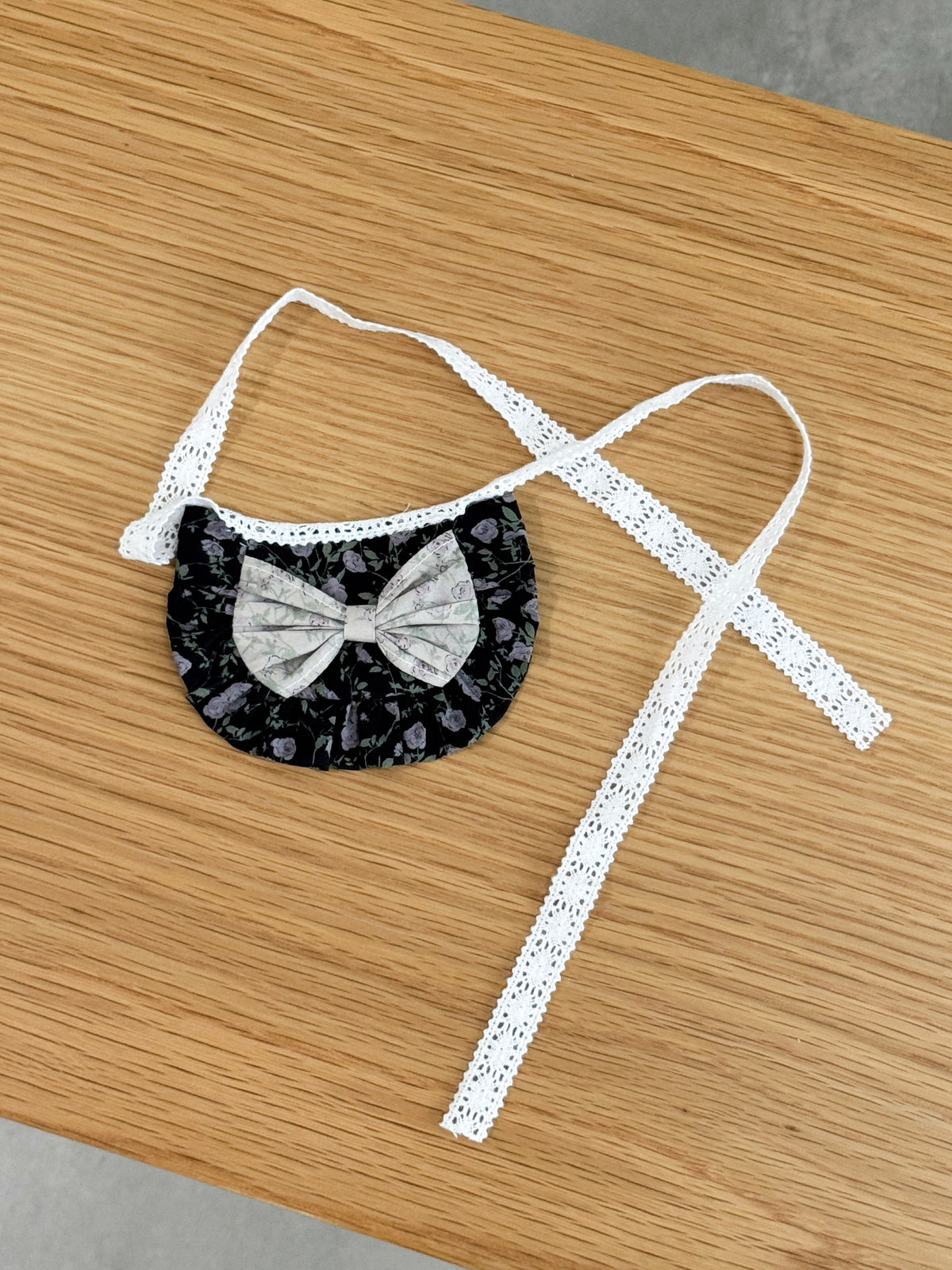 Black floral ruffle bib for plush toys with contrasting floral bow and white lace ties