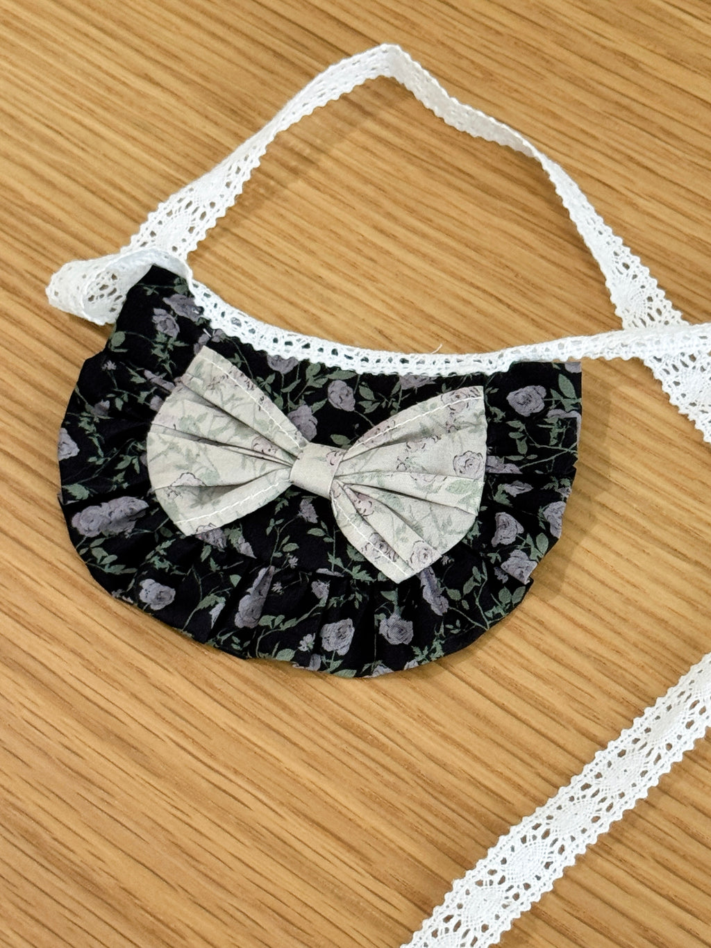 Close-up of black floral ruffle bib for plush toys with contrasting floral bow and lace tie fastening