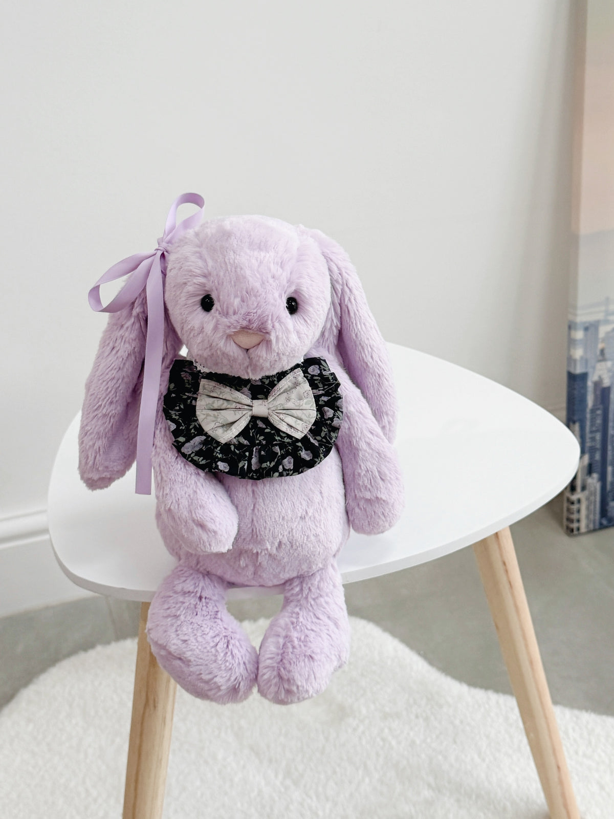 Purple plush bunny wearing a black floral ruffle bib with contrasting floral bow and lace ties