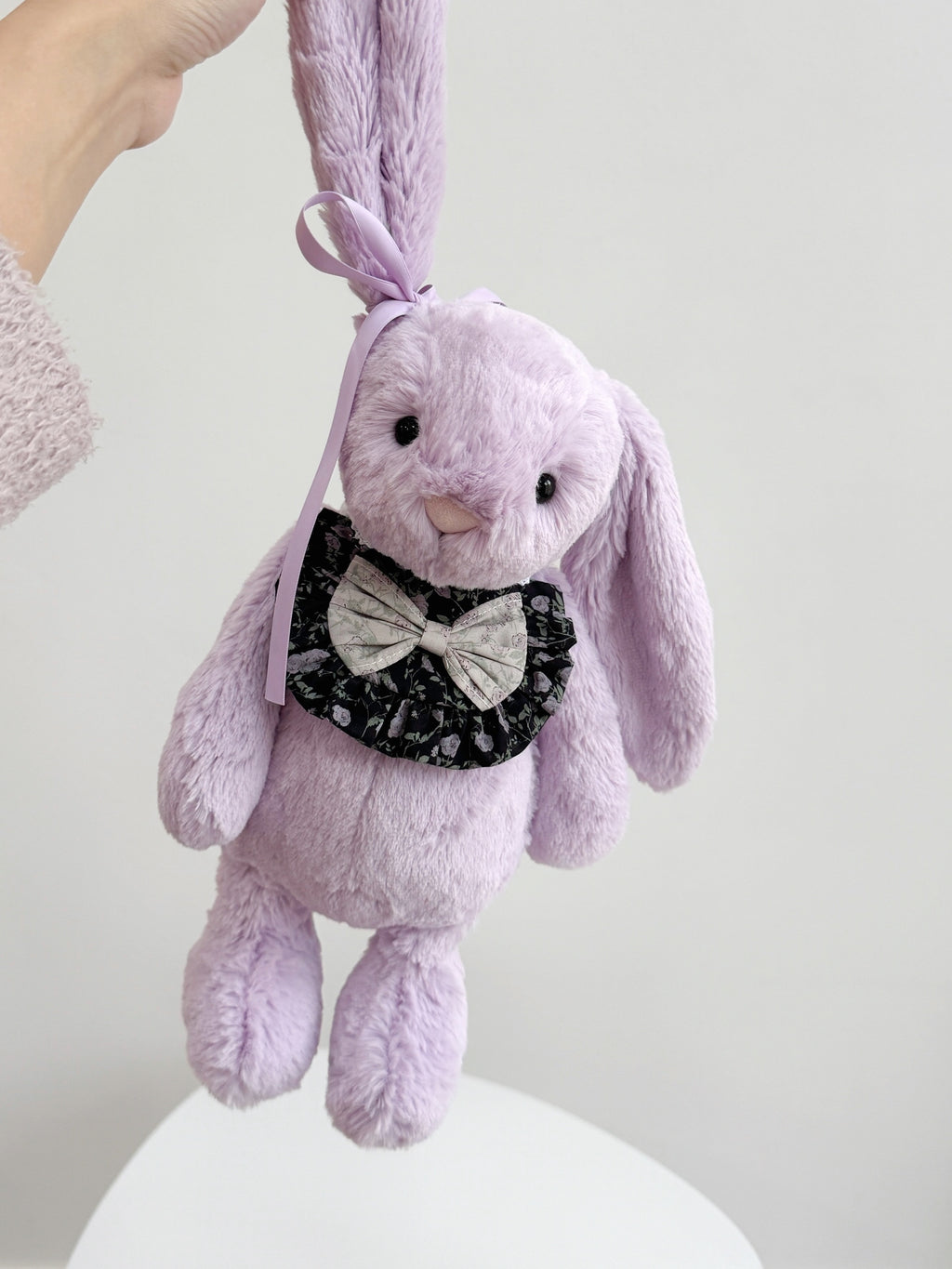 Purple plush bunny wearing a black floral ruffle bib with contrasting floral bow and adjustable lace ties