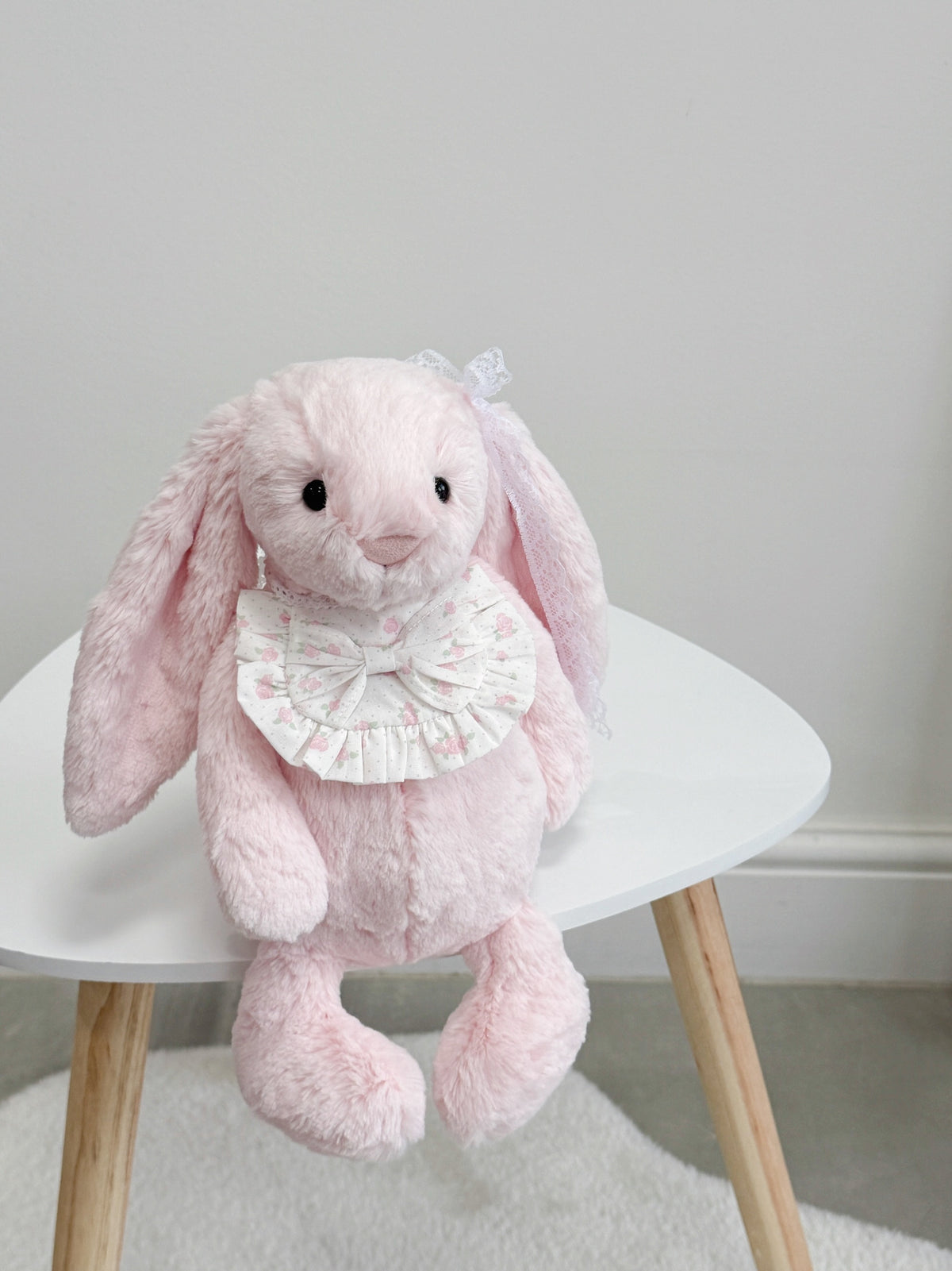 Pink plush bunny wearing a pink rose ruffle bib with matching floral bow and white lace ties